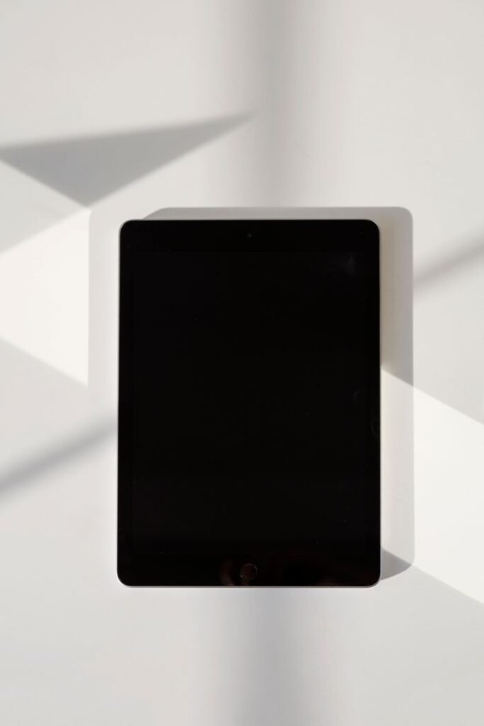 A digital tablet with a blank screen lies on a white surface in natural light.